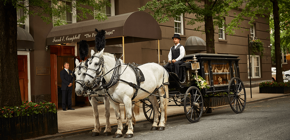 A horse-drawn hearse arrives at Frank E. Campbell Funeral Chapel.  It awaits a casket on its way to a nearby NYC cemetery.